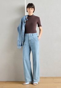 Braun gestreifter Kurzarm-Top, hellblaue hochtaillierte weite Jeans, Jeansjacke über eine Schulter gelegt und hellblaue offene Schuhe mit Absatz.