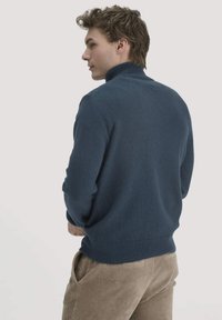 Dunkelblaues Rollkragenpullover aus strukturiertem Strick, mit taillierter Passform und geripptem Saum. Kombiniert mit hellen Cordhosen.