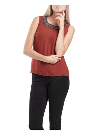 Rdzawy bezrękawnik z naszywkami na dekolcie. Gładki materiał, luźny krój i proste wykończenie; zestawiony z dopasowanymi czarnymi spodniami.