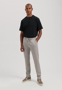 Črna majica s kratkimi rokavi v kombinaciji s svetlo sivo hlačami na vrvico in sivo športno obutvijo. Hlače so slim fit ter imajo subtilno teksturo.