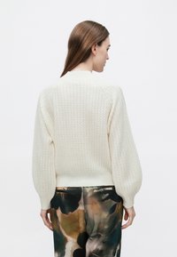 Kremfarvet strikket sweater med tekstureret mønster, ribstrikkede manchetter og kant. Stylet med løse, farverige bukser med mønster.