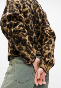 Svetr s leopardím potiskem vyrobený z měkkého, chlupatého materiálu s černými akcenty a zkráceným střihem, doplněný světle zelenými džínami s zadní kapsou.