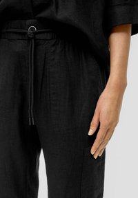 Czarne lniane spodnie z elastycznym pasem, z detalem guzików i kieszeni. Gładka tekstura, luźny krój i prosta nogawka.