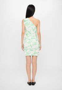 Robe mini à une épaule en blanc avec un motif de feuilles vertes. Tissu doux et ajusté avec des détails froncés sur la jupe, longueur au-dessus du genou.