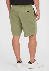 Grüne Shorts mit elastischem Bund, Gesäßtaschen und entspannter Passform, kombiniert mit weißen Sneakers, die ein schwarzes Logo an der Ferse haben.