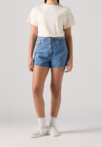 Camiseta blanca de manga corta y shorts de mezclilla azul de tiro alto. Los shorts tienen un diseño clásico de cinco bolsillos. Zapatillas blancas y calcetines de caña media.