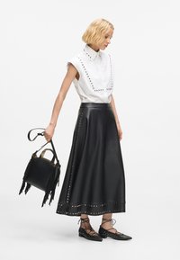 Fekete bőrszoknya studdal díszítve, fehér inggel, ami fekete studdal van ellátva. Kicsi fekete kézitáskát tart a rojtos részével.