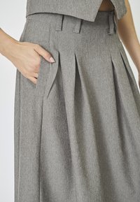 Gray pleated skirt with side pockets, made of textured fabric. Features tailored waistband and sharp creases for structured design.
