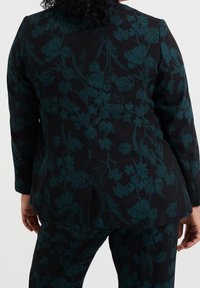 Svart blommig kavaj med mörk teal blommönster, strukturerad passform, lång ärm och en enda ryggslits för ökad rörlighet.