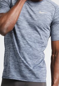 Navyblå träningsskjorta med en texturerad, horisontell mönstring och korta ärmar. Har en liten, ljusgrå Nike-logotyp på bröstet.