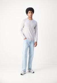 Light gray long-sleeve shirt paired with light blue jeans and white sneakers with gray accents, standing against a plain background.