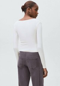 Witte langemouwen shirt met een brede halslijn. Gecombineerd met grijze denim broek, met achterzakken en een rechte pijp.