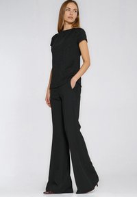 Czarny pleciony top z krótkimi rękawami w połączeniu z czarnymi, szerokimi spodniami o wysokim stanie. Oba elementy charakteryzują się prostymi liniami i minimalistycznymi detalami.