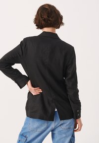 Schwarzer Leinenblazer mit taillierter Passform, einzelnen Schlitz hinten und knöpfbaren Manschetten, kombiniert mit hellblauen Cargo-Hosen.