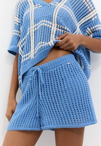 Conjunto de loungewear de color azul claro, con un top de tejido suelto y patrón abierto, y pantalones cortos a juego con cintura elástica y cordón ajustable.