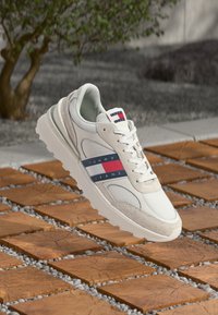 Bijela tenisica s mrežastim i antilop akcentima, koja ima crveno-bijelu-plavu prugastu logotip sa strane. Teksturirana gumena sola, dizajn s vezicama.