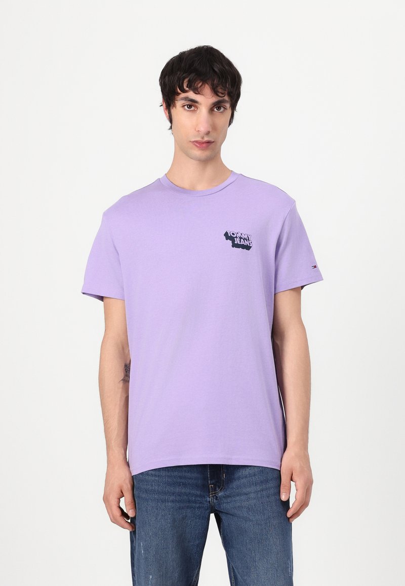 Šviesiai violetinė medvilninė marškinėliai su trumpomis rankovėmis, ant kairės krūtinės puikuojasi juodas "Tommy Jeans" logotipas, o ant rankovės yra mažas logotipo akcentas.