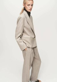 Traje gris claro a rayas con un blazer cruzado a medida y pantalones de pierna ancha, combinado con un suéter de cuello alto negro por debajo.
