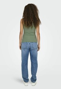 Groen getailleerd tanktop met gegolfde zoom, gecombineerd met blauwe hoge taille rechte jeans en witte sneakers. Krullend haar zichtbaar.