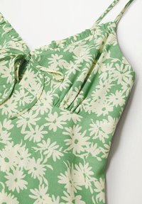 Vestido floral verde con patrones de margaritas blancas, tejido suave, tirantes ajustables y detalles fruncidos alrededor del escote.