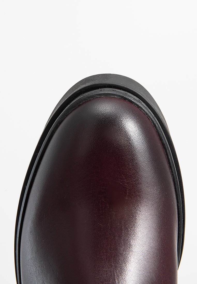 Botín de cuero burdeos con puntera redondeada, textura suave y suela de goma negra. Presenta un brillo sutil y un detalle de borde cosido.