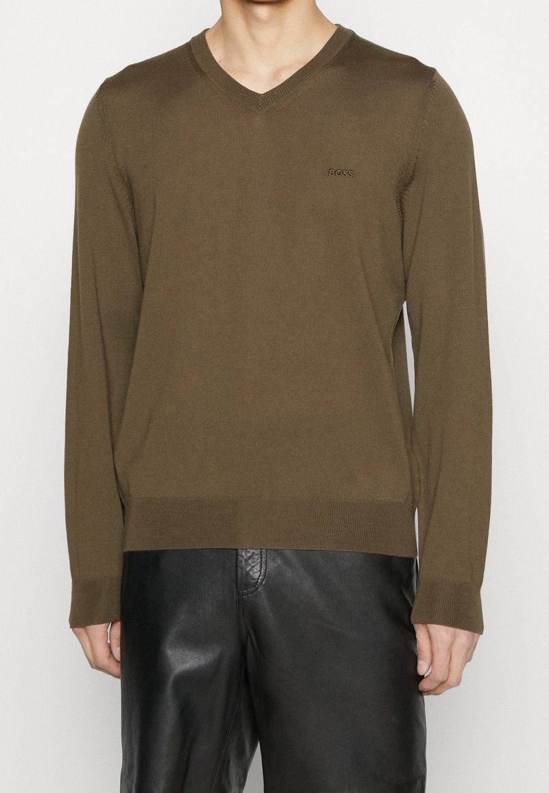 Brauner V-Ausschnitt-Pullover mit langen Ärmeln, aus einem glatten Strickstoff gefertigt. Mit einem dezenten Logo auf der Brust sowie gerippten Bündchen und Saum.