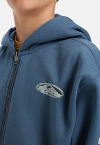 Blauwe zip-up hoodie gemaakt van zachte stof, met een logo-opdruk aan de voorkant, een trekkoord capuchon en ribbeltrim op de manchetten en de zoom.