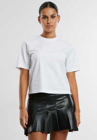 Tricou alb din bumbac cu mâneci scurte, guler rotund și o croială lejeră, asociat cu o fustă mini plisată din piele ecologică neagră.