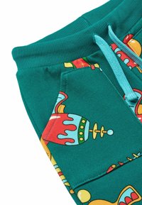 Los pantalones de chándal en color verde azulado presentan coloridos patrones festivos, incluyendo diseños de adornos y dulces, con un cordón ajustable y un bolsillo lateral visible.
