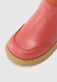 Bota de tornozelo rosa em pele com uma textura suave, bico redondo e costura em contraste. Apresenta uma sola de borracha com um acabamento bege.