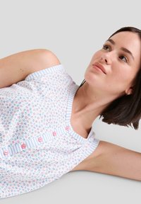 Top sin mangas para mujer con un patrón floral en rosa y azul sobre un fondo blanco; cuenta con un ribete azul a rayas y botones rosas.