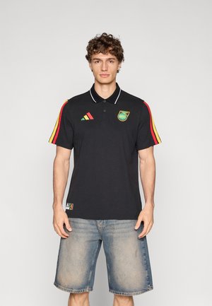 Fekete, rövid ujjú galléros póló, kontrasztos piros, sárga és zöld csíkokkal és egy emblémával. Hozzá illő, kifakult kék farmerral.