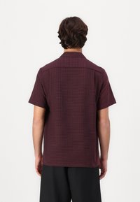 Korte mouwen, bordeaux shirt van textiel met een subtiel patroon. Heeft een klassieke kraag en een iets ontspannen pasvorm.