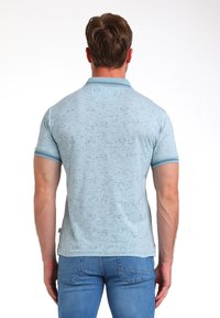 Camisa polo azul claro con un patrón texturizado, mangas cortas y un cuello de color sólido. Combinada con jeans azules.