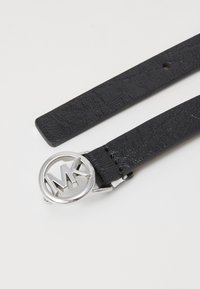 Curea din piele neagră cu un finisaj texturat, cataramă circulară argintie cu logo-ul „MK” și sistem de închidere cu un singur vârf.