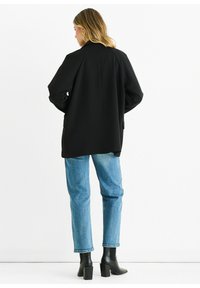 Black oversized blazer, textured fabric, slightly structured design. Paired with light blue denim, ankle-length, relaxed fit jeans and black heeled boots.