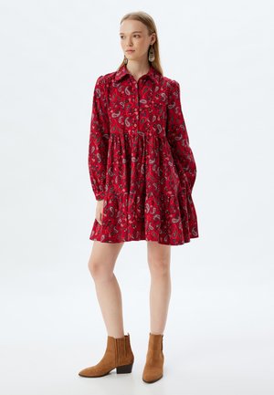 Rotes Paisleymuster-Kleid mit langen Ärmeln, Kragen, Knopfleiste und gestuftem Rock. Kombiniert mit braunen Wildleder-Stiefeletten.