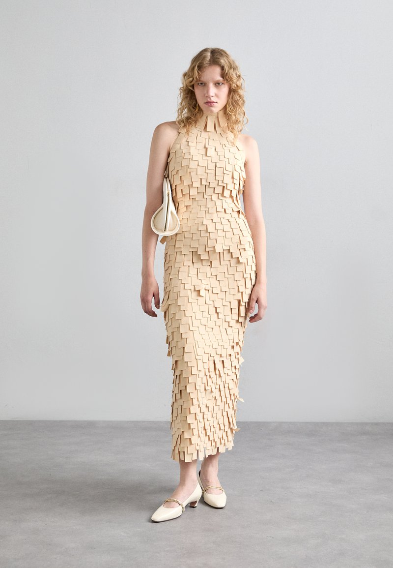 Knee-length beige dress featuring a textured design with layered square elements. A matching handbag and light-colored shoes complete the look.