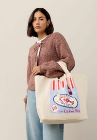 Taška cez rameno v krémovom plátne s farebnou grafikou homára a citróna, s ružovými a červenými pruhovanými akcentmi na vrchu.