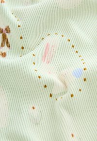 Textil s jemně zelenou žebrovanou tkaninou s měkkou strukturou, zdobený malými hnědými tečkami a ilustracemi pastelových zvířat.