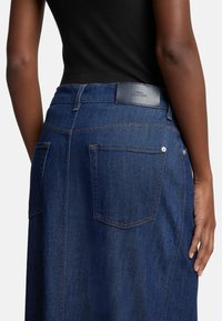 Denim skjørt i mørk blå, med høy midje, to baklommer og subtil sømdetalj. Teksturert stoff med lærbelteetikett.