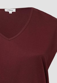 Bordeaux korte mouwen top met een V-hals. Gemaakt van zachte stof, met een gladde textuur en eenvoudige stikdetails. Merktafel zichtbaar.