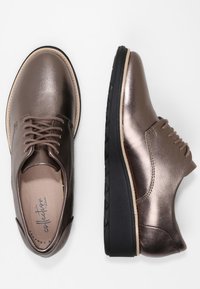 Bruine metalen veterschoenen met een glad leren bovenwerk, contrasterende zwarte rubberen zool en minimalistisch ontwerp.