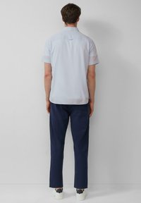 Helles blaues Kurzarmhemd mit feiner Textur und einem Rückenbesatz. Kombiniert mit dunklen marineblauen Hosen und weißen Sneakern.