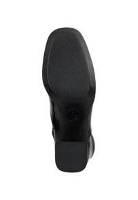 Suola di scarpa in pelle nera con grip in gomma testurizzata, forma arrotondata e un leggero tacco con un emblemma circolare vicino al blocco del tacco.