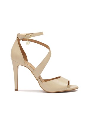 Beige leather high-heeled sandal with cross straps, open toe design, and a small gold accent on the ankle strap. Smooth texture.