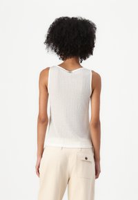 Top senza maniche a coste in beige chiaro con schiena a V, caratterizzato da un bottone metallico decorativo sul collo e una silhouette aderente.