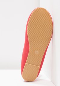 Chaussure plate rouge posée sur une surface blanche, montrant sa semelle nervurée marron clair avec le numéro de taille 37 embossé au centre.