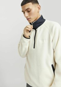 Fleece-Pullover in Creme mit einem Marinekragen, Reißverschluss am Hals und schwarzen Akzenten. Verfügt über ein dezentes Logo und eine weiche, strukturierte Oberfläche.
