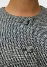 Šedá textilie s potiskem houndstooth, s kulatým zapínáním na knoflík a jemnou strukturou, na bundě s vysokým límcem.